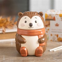 Ceramic hedgehog-shaped container with a scarf on a wooden surface.