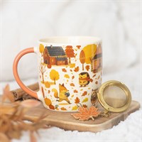 Mug with autumn-themed design on a wooden coaster with a tea ball and leaf decoration.