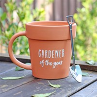 Terracotta mug with 'Gardener of the Year' text on a wooden surface with a garden tool.